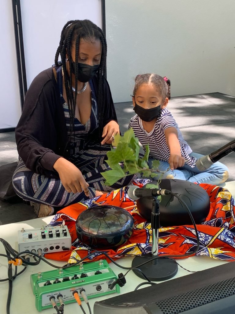 Bring the Cool! Honoring Juneteenth with Brooklyn Museum 5 Rena Anakwe guides a child holding a leafy twig through the exploration of sound bath instruments.