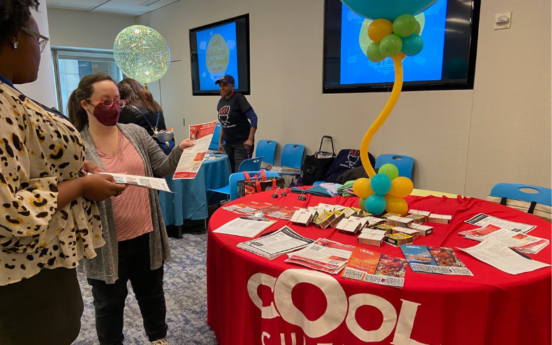 Two adults look at a booklet next to a table with art supplies and a sign "Cool Culture"